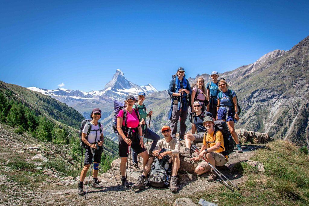 A group of hikes in the Alps on Chamonix to Zermatt Haute Route trek with snow capped peaks behind them