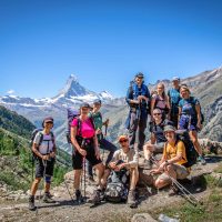A group of hikes in the Alps on Chamonix to Zermatt Haute Route trek with snow capped peaks behind them