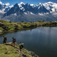 hikers by famous reflecting lake, aiguilles rouge Tour du mont blanc trekkers above Chamonix with alpine lake and snowy peaks in the horizon.