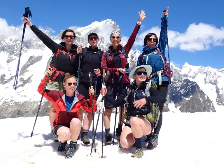 Six female TMB hikers posing on a snow with snowy mont blanc in the background.