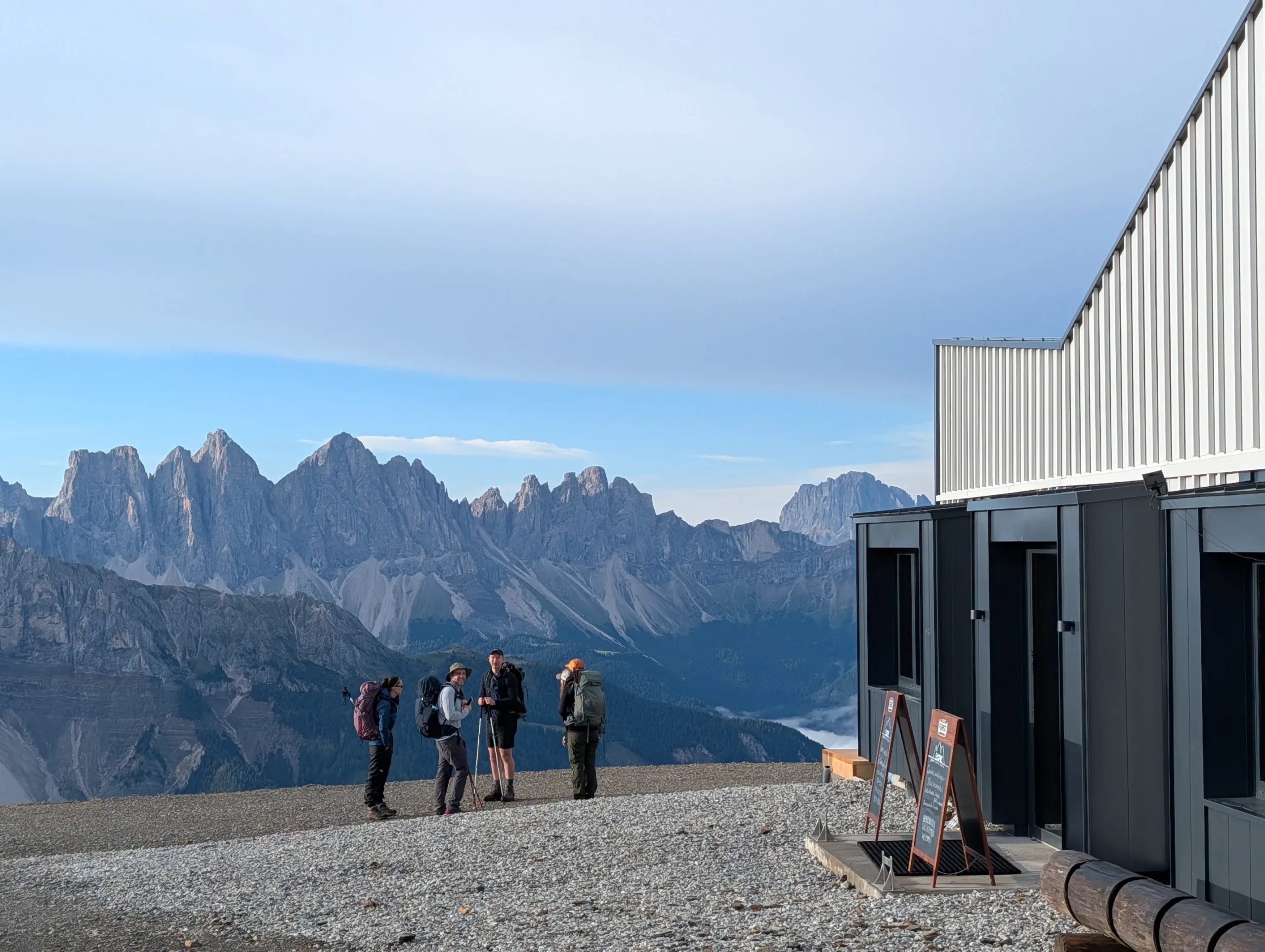 AV2 Hikers standing by a modern Plosehütte mountian hut with steep Dolomites peaks in the background on the Alta Via 2 trek