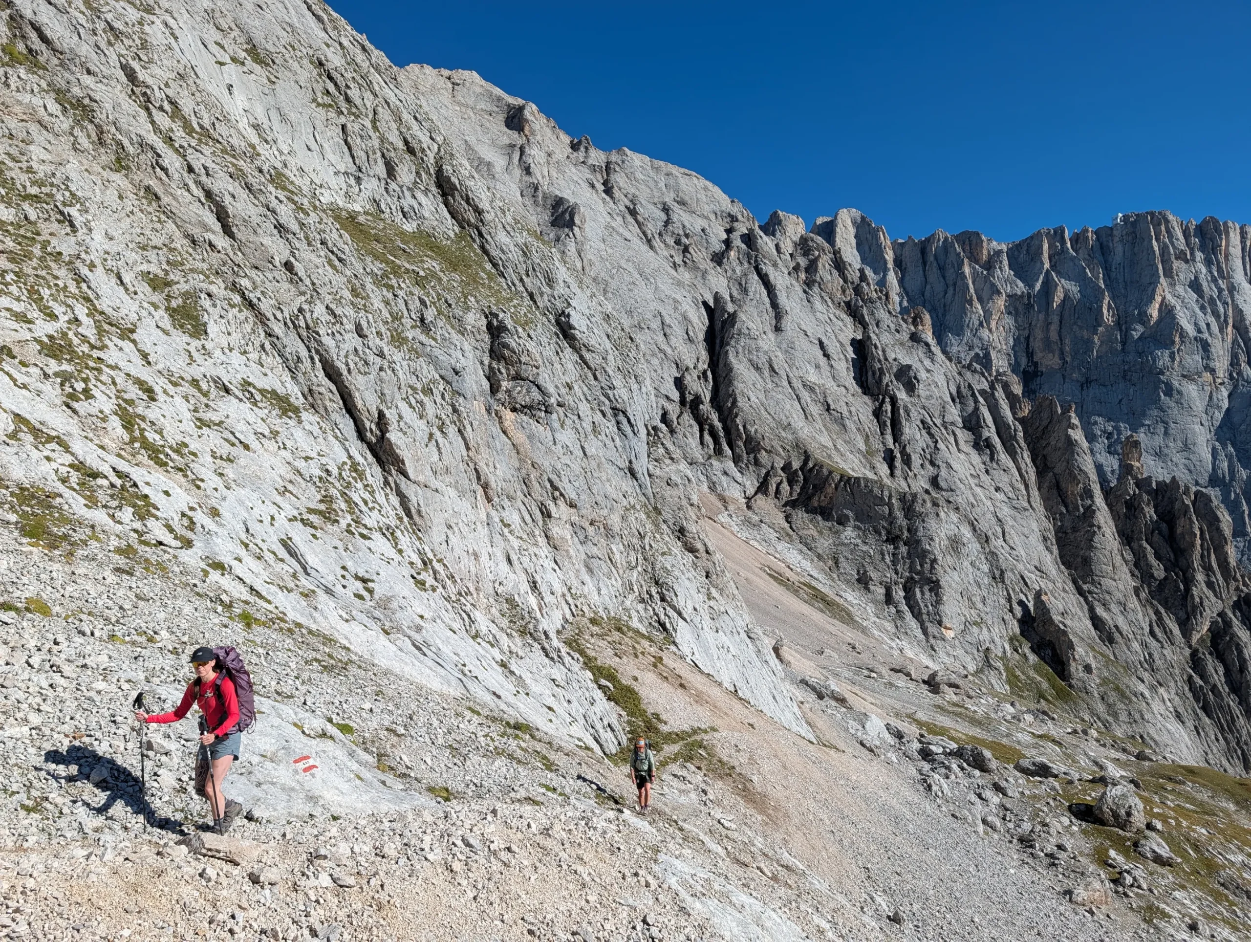 Hiker on rocky trail of AV2 with steep cliffs of Dolomites behind her